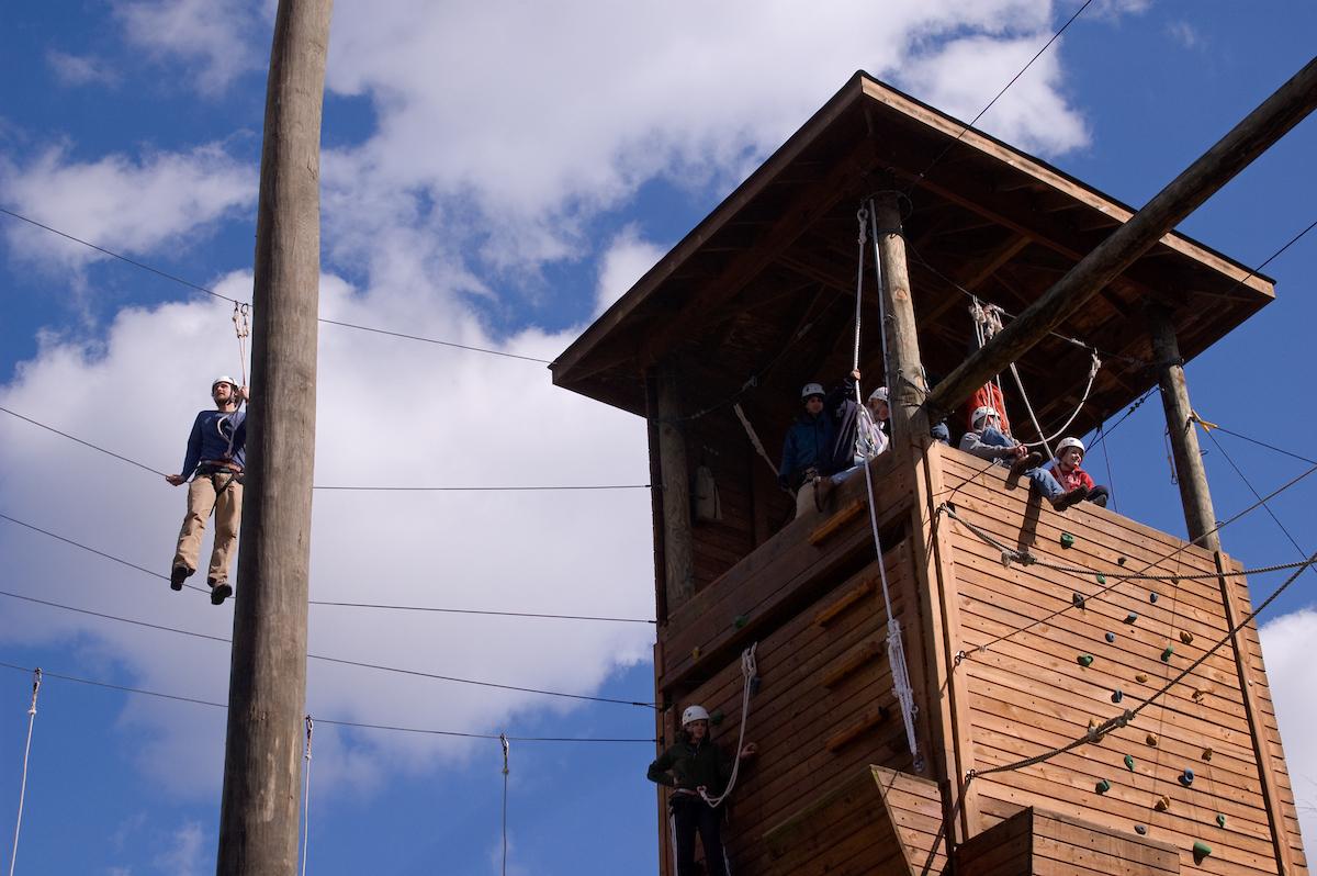 Students sit in a high ropes course tower, atop a rock wall at Ohio University