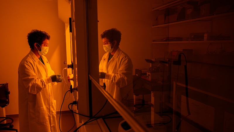 An OHIO researcher works in a lab and the reflection is shown in a window in the Russ Research Opportunity Center