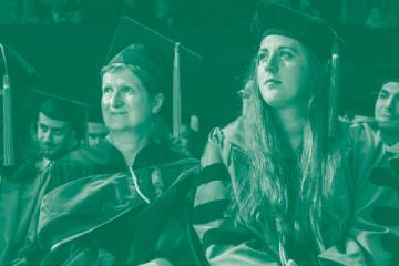 Faculty members dressed in academic regalia sit in an audience