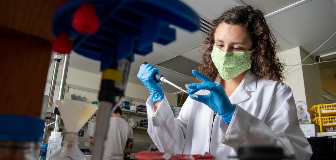 Female student conducts a science experiment in a lab while wearing a face mask
